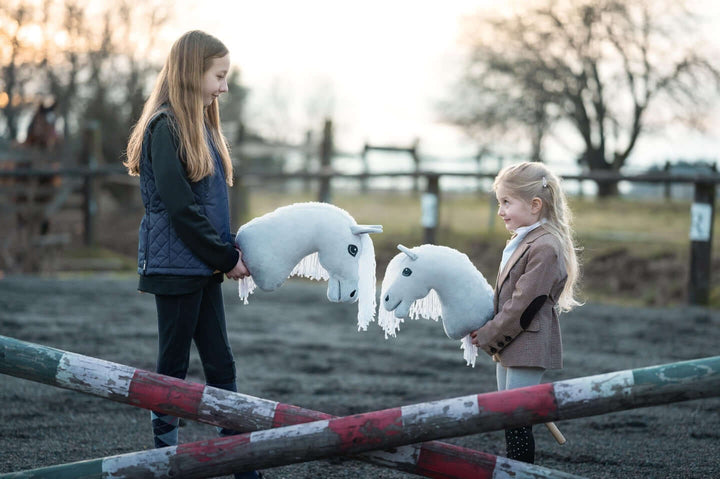 Két gyerek fehér Hobby Horse lovakkal festett akadályok mellett egy szabadtéri pályán