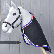 Szürke Hobby Horse ló fekete kötőfékben, fekete steppelt szállítótakaróban kék, piros és fehér szegéllyel, háromnegyedes nézetből