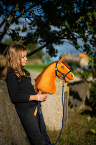 Girl in a black jumper leaning on a stone block under a tree, holding Hobby Horse Wendy on a navy lead rope
