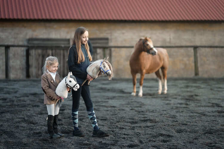 Két gyerek Hobby Horse lovakat visz egy szabadtéri pályán, egy póni mellett