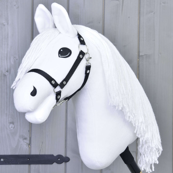 Fehér Hobby Horse ló fekete kantárral és hosszú, fehér fonalsörénnyel, boton, szürke fafal előtt.