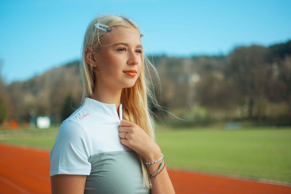 Blonde girl on a running track in a white and grey sports shirt with a zip collar and pink LarDen print