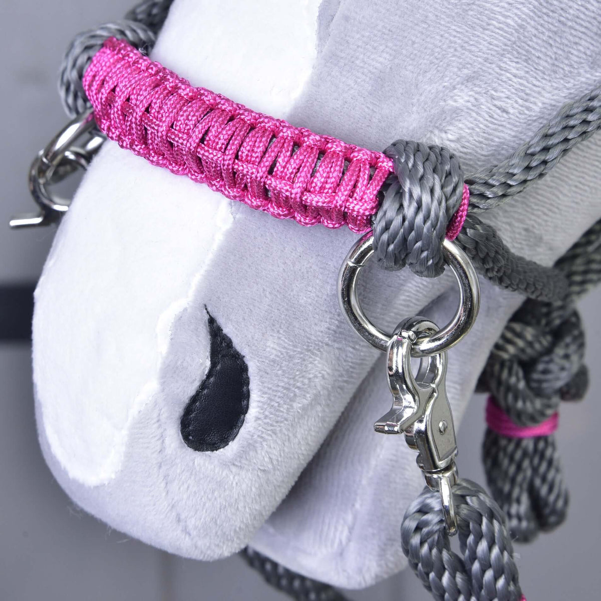 A rózsaszín tekert orrszíj közelről ezüst karikával és karabinerrel egy Hobby Horse ló szürke csomózott kötőfékén