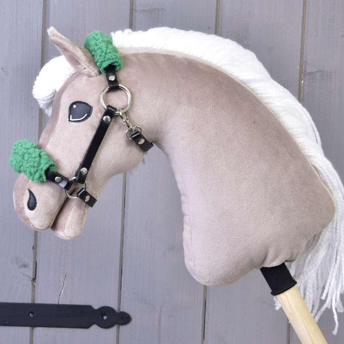 Beige Hobby Horse with a white yarn mane wearing the black leatherette halter with green fur on the noseband and crown