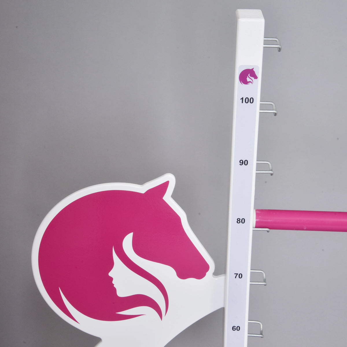 Közeli kép a szárnyon lévő rózsaszín lófej- és lánysziluettről a skála mellett, egy rózsaszín akadályrúd 80 cm-en