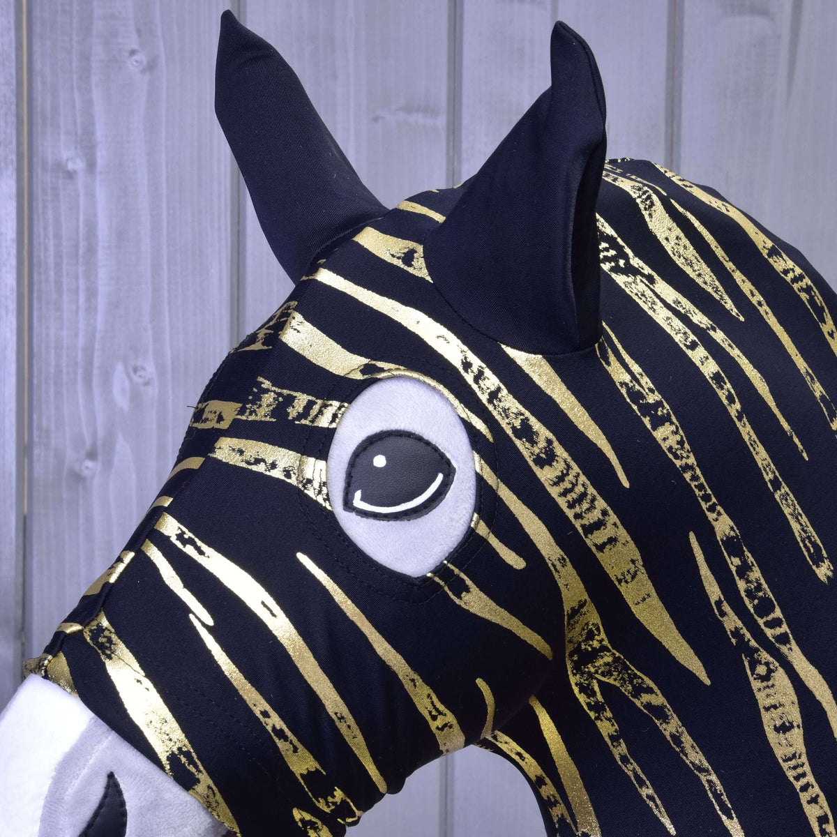Close-up of the gold zebra stripes, black ears and round eye opening of the Lycra protective suit on a Hobby Horse