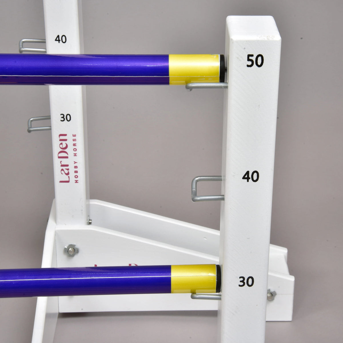 Sárga végű kék akadályrudak egy alacsony oszlop 30 és 50 cm-es tartókampóin, mögöttük a magas oszlopon LarDen felirat