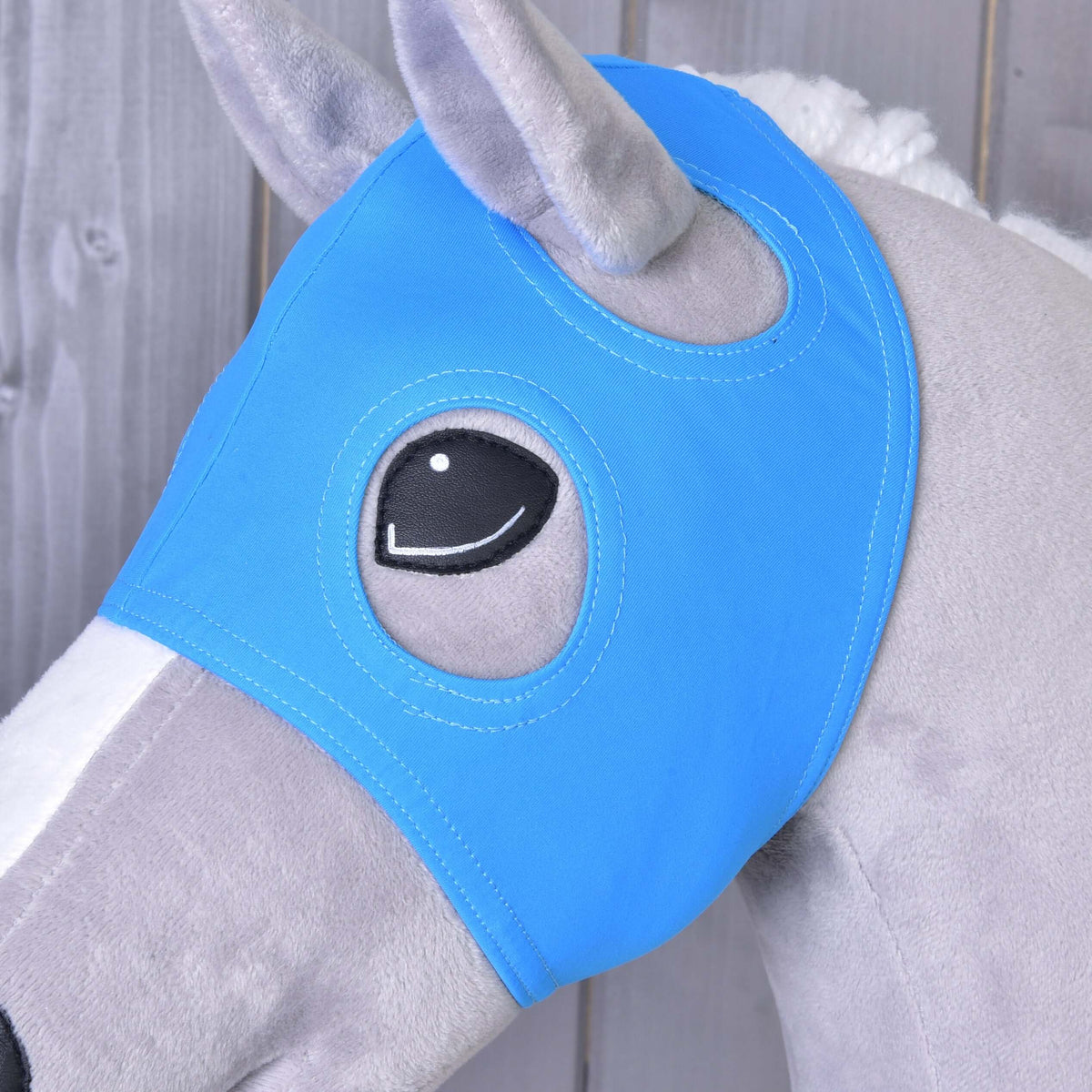 Close-up of the Horse Mask without ears Sky on a grey Hobby Horse, the plush ear and black eye framed by the openings