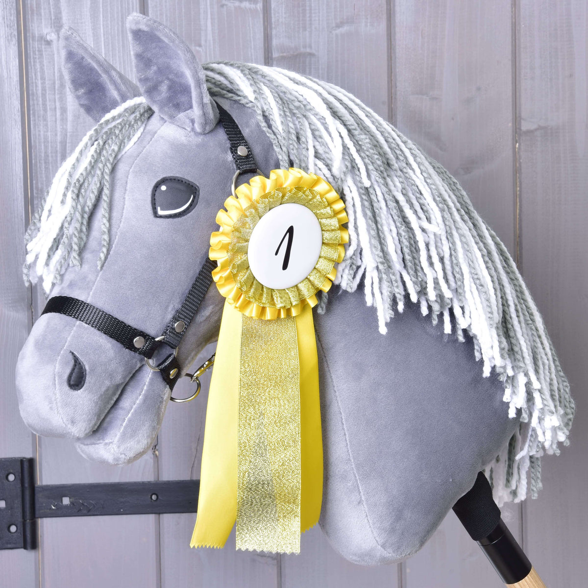 First place: the yellow and gold rosette with number 1 pinned to the neck of a grey Hobby Horse with a black halter