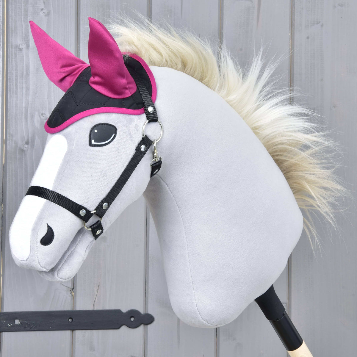 Krémszínű sörényű, világosszürke Hobby Horse ló fekete kötőfékben, a fekete-magenta Thermo Sky fülvédővel