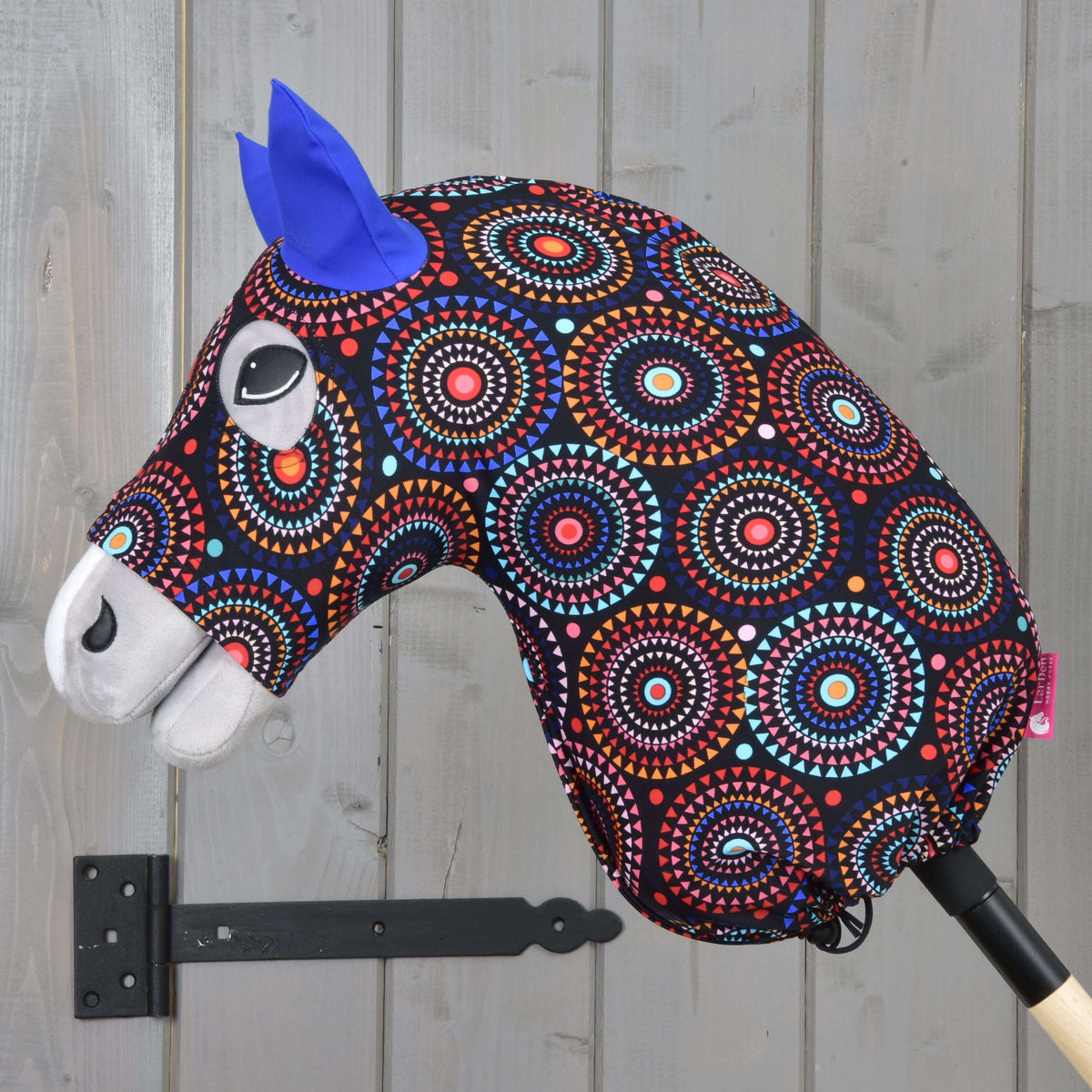 Side view of a grey Hobby Horse in the Protective suit Alice, colourful mandala print gathered by a drawstring at the stick