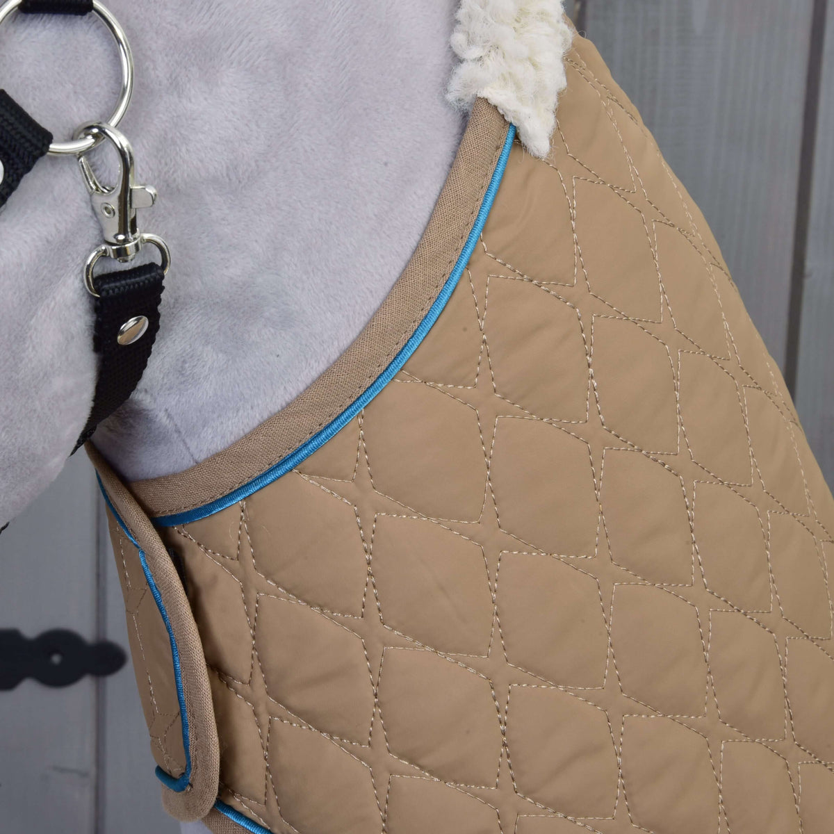 Close-up of the beige diamond-quilted blanket with blue piping and cream sherpa collar at a grey plush neck
