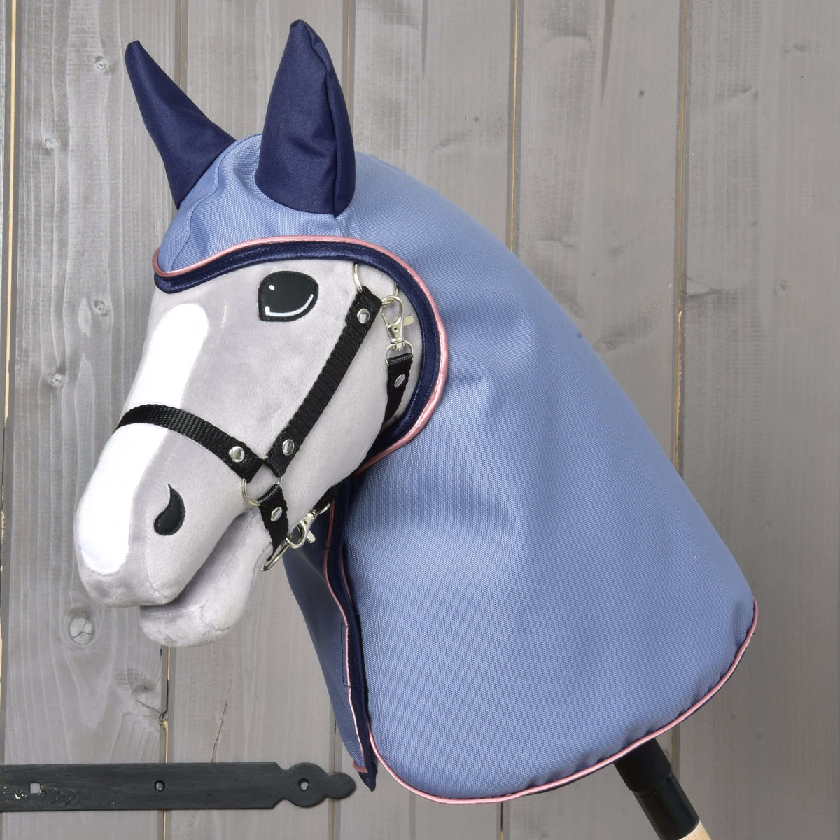 Szürke Hobby Horse ló fekete kötőfékben, a kapucnis Bloom esőtakaróban sötétkék fülekkel, világoskék színben, rózsaszín paszpóllal
