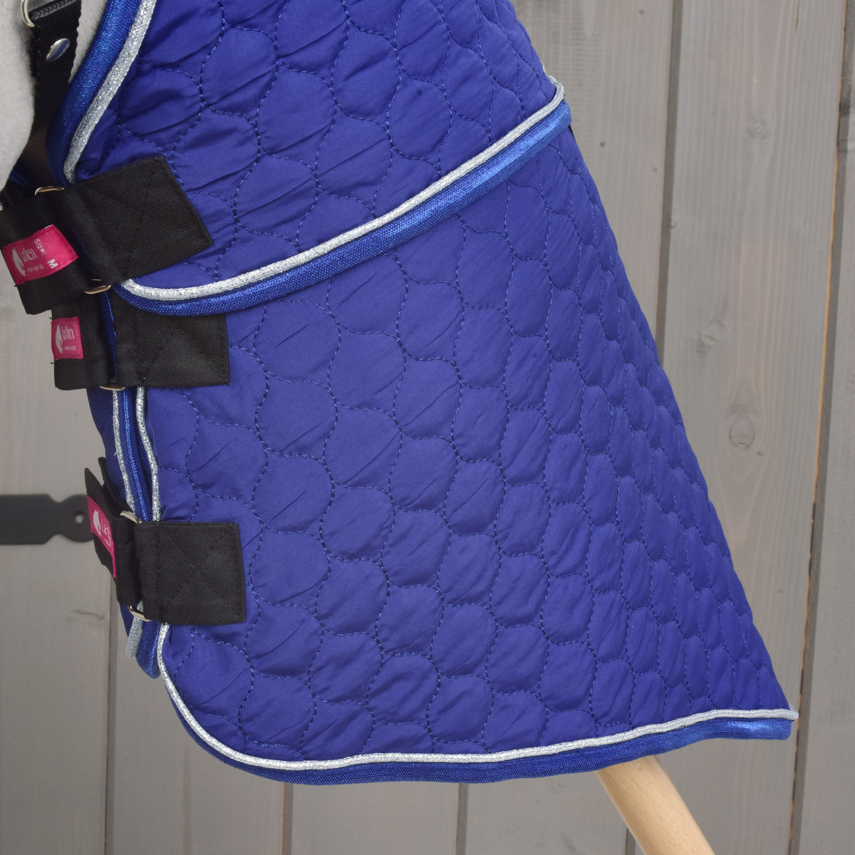 Lower part of the Bluebell blanket from the side, circle quilting down to the silver-piped hem above the wooden stick
