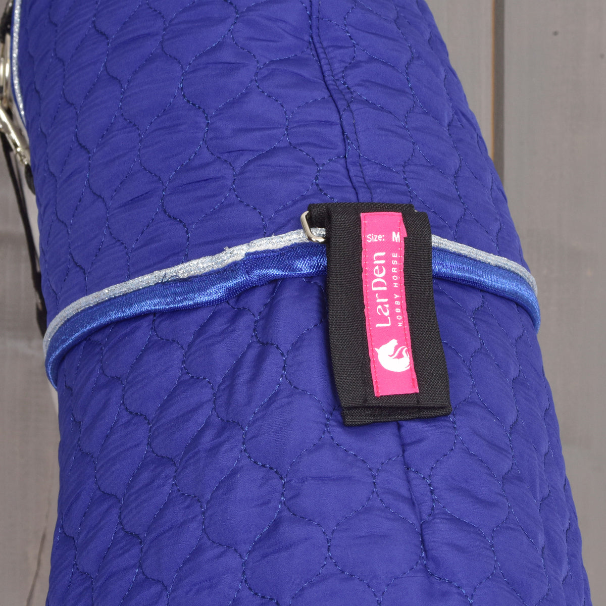 Pink LarDen Hobby Horse label on a black strap of the Bluebell neck cover, above blue and silver piping
