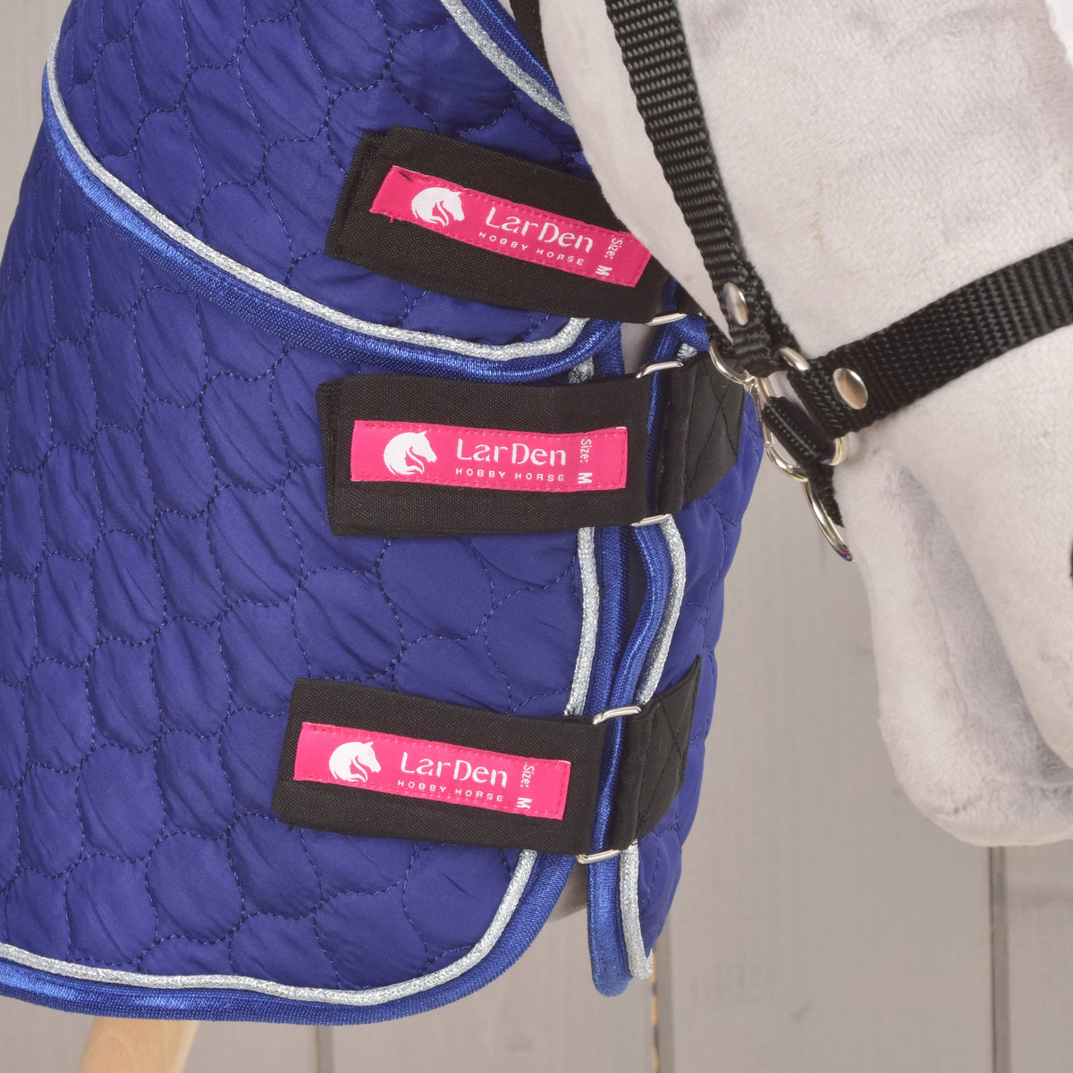 Grey Hobby Horse in a black halter with the Bluebell blanket fastened by three black straps with pink LarDen labels