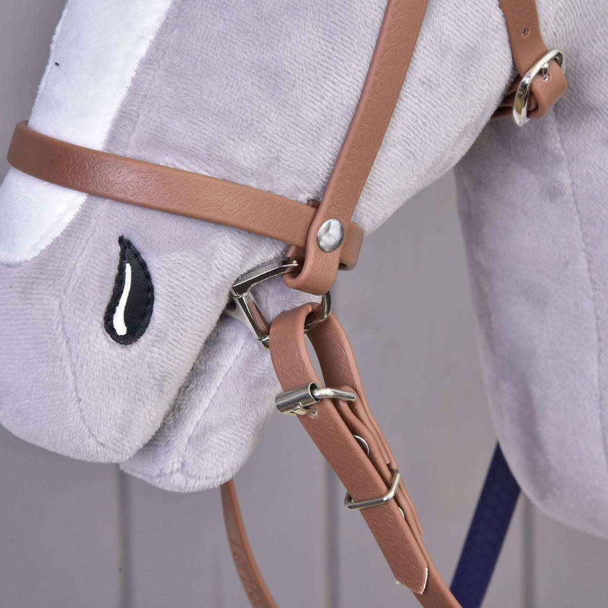 A világosbarna műbőr orrszíj közelről ezüst csatokkal és szárcsatlakozóval egy szürke Hobby Horse ló orrán