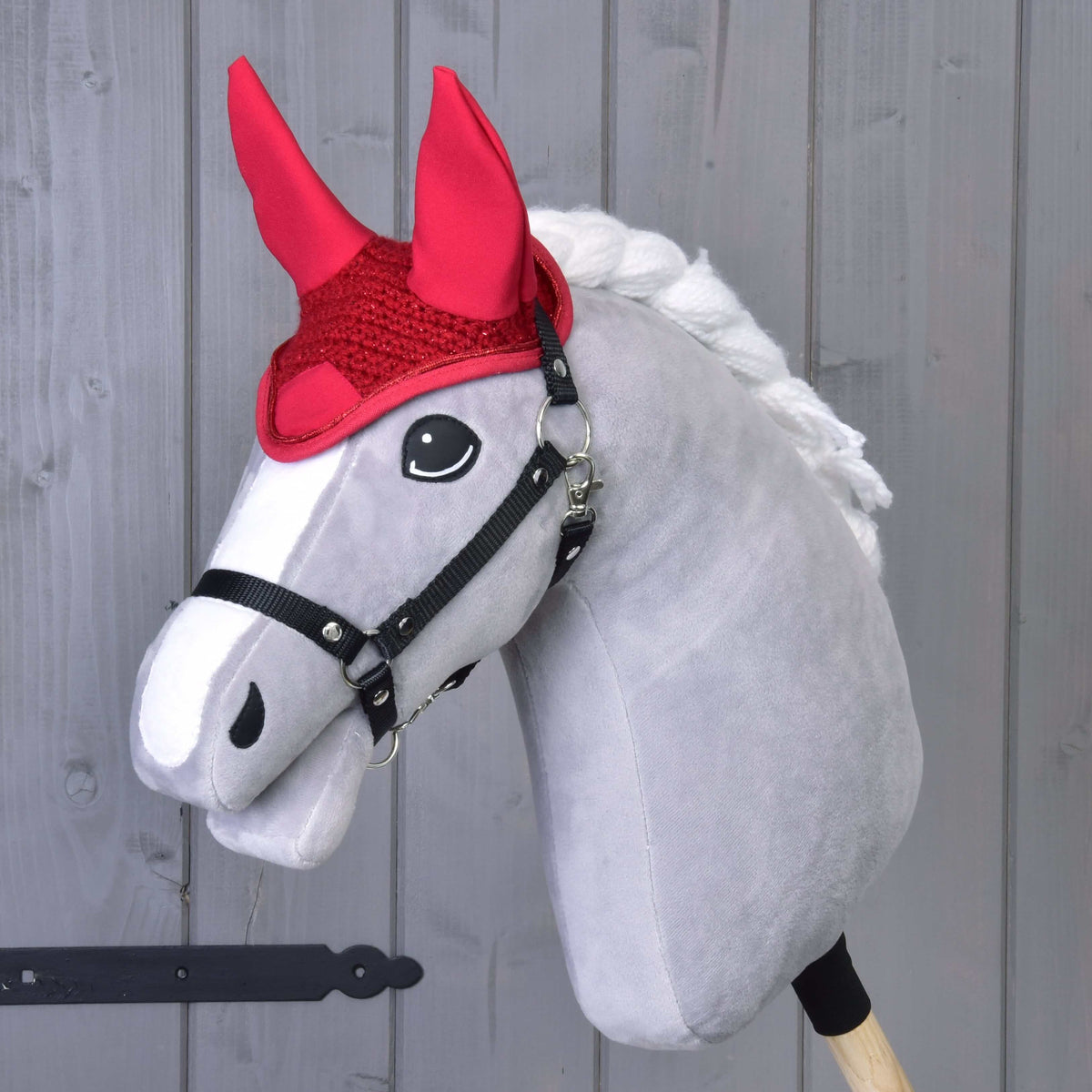 Szürke Hobby Horse ló fekete kötőfékben, rajta a piros horgolt fülvédő magas textilfülekkel