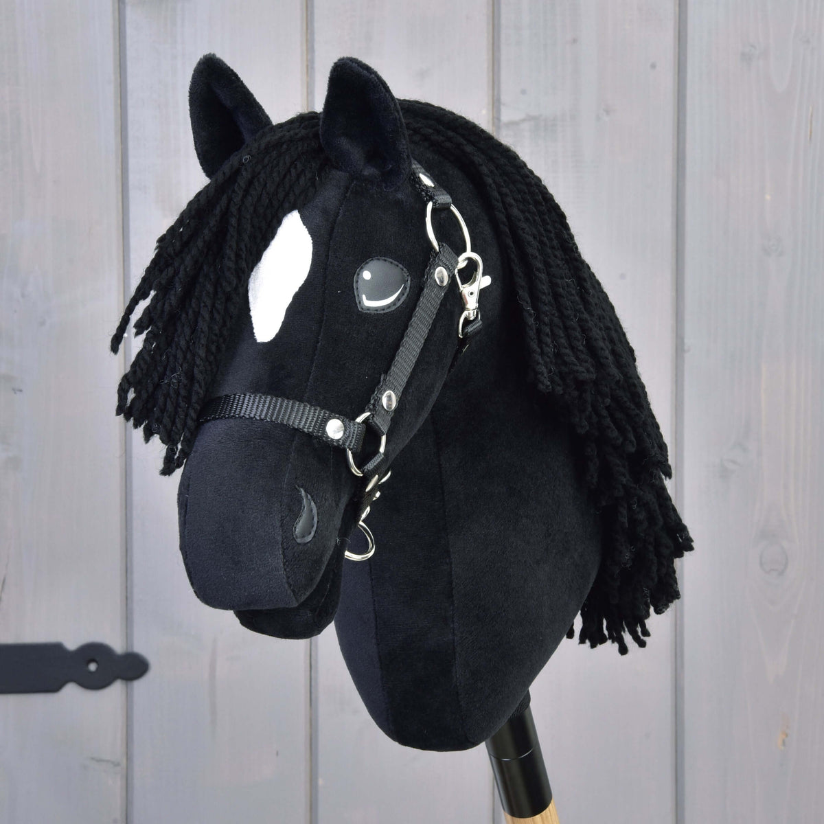 Front view of Hobby Horse Cloony with a black yarn forelock, white star and the black halter on a light wooden wall