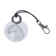 A kerek fényvisszaverő kulcstartó hátoldala egy boton lévő, göndör sörényű szürke Hobby Horse ló rajzával