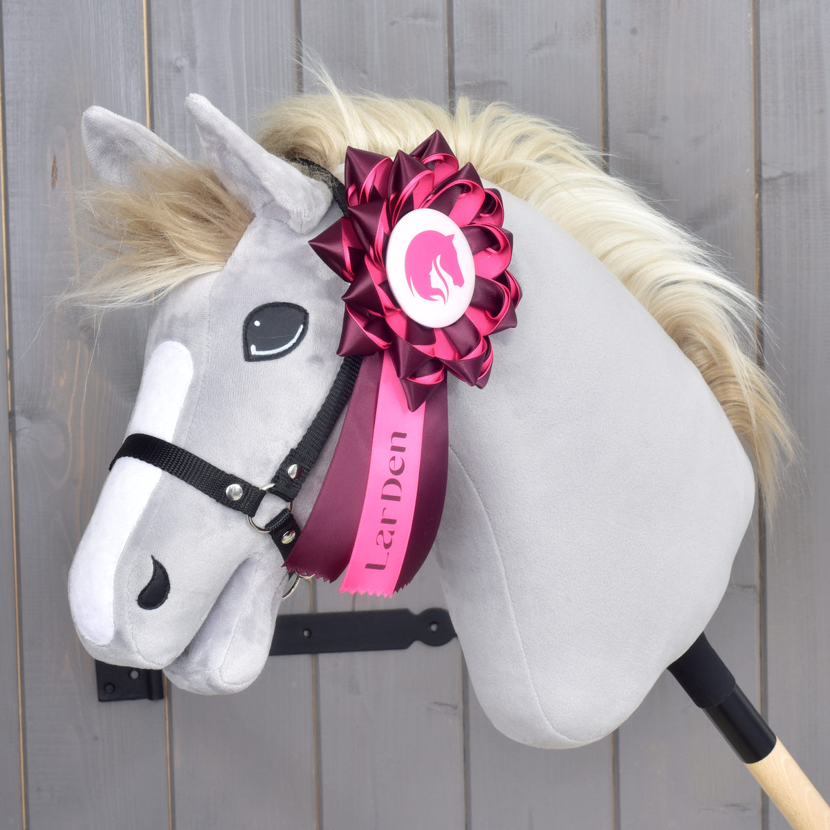 Hobby Horse Ribbon Raspberry Rose on the black halter of a grey plush head, its pink middle tail printed with LarDen