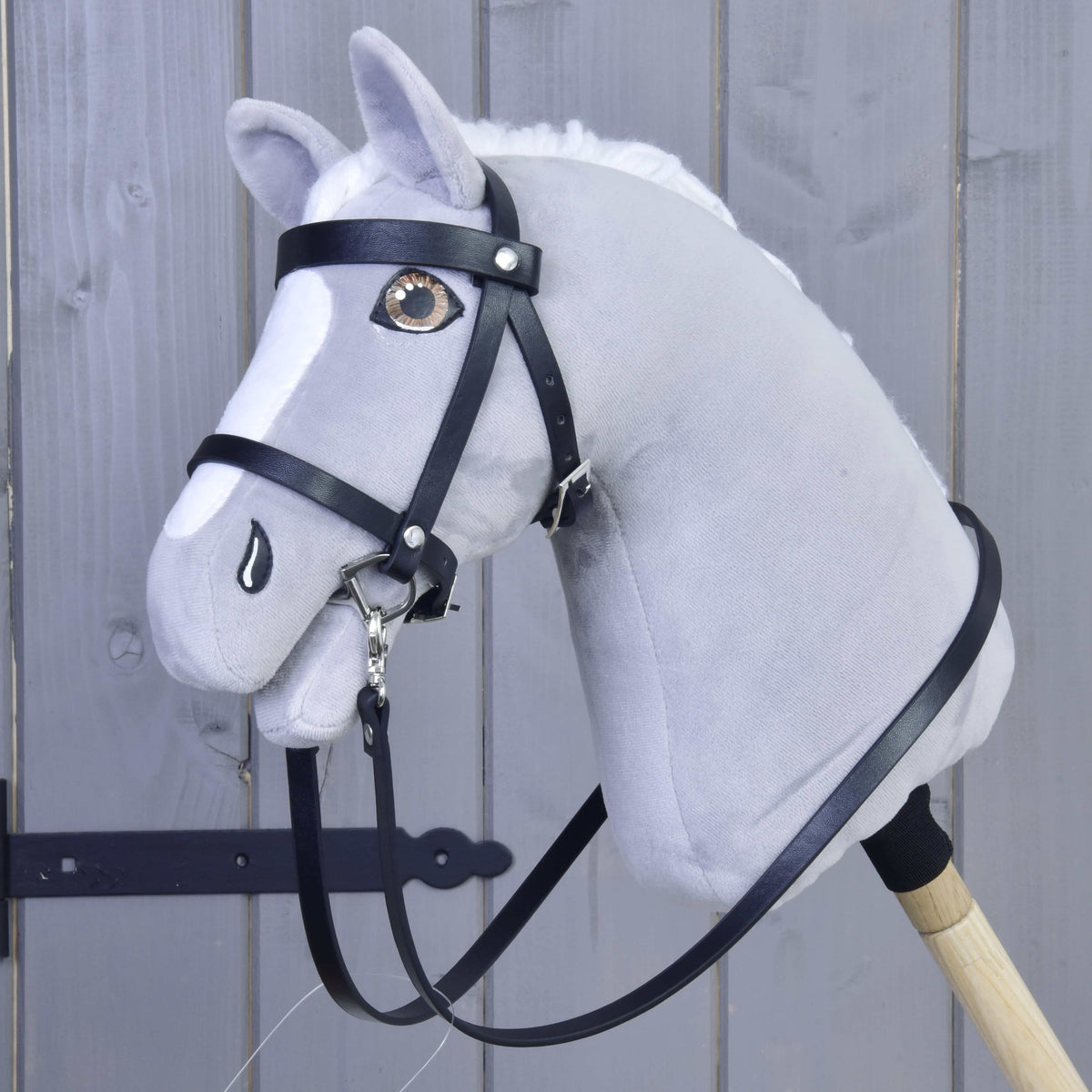 Grey Hobby Horse with brown eyes wearing the Set Basic bridle with long black reins, on a wooden stick