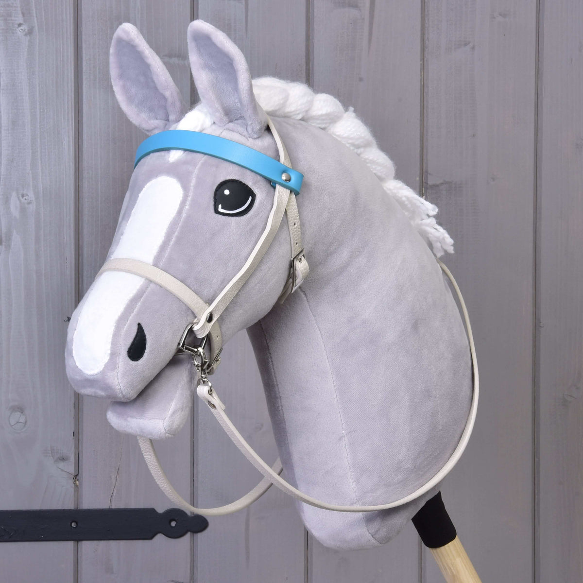 Grey Hobby Horse in the cream leatherette bridle with aqua blue browband and long cream reins, three-quarter view