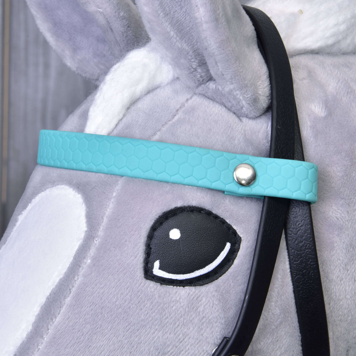 Közeli kép: méhsejtmintás türkiz homlokszíj ezüstszínű szegeccsel egy szürke Hobby Horse ló szeme mellett