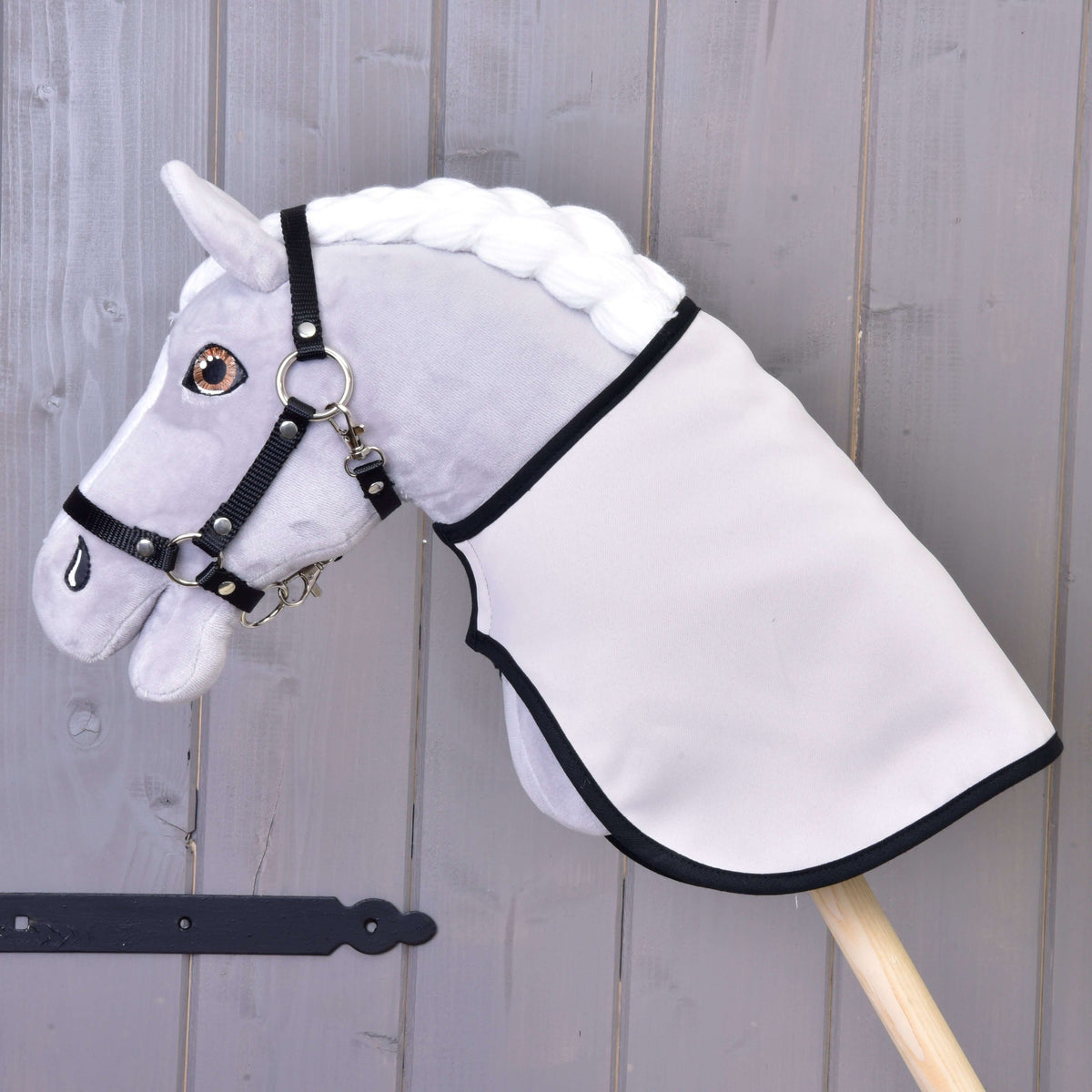 A grey plush Hobby Horse in a black halter wears the blanket turned to its plain light side with black trim