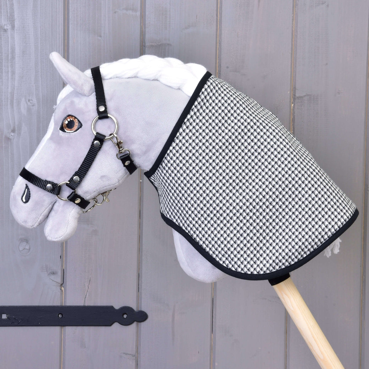 A grey plush Hobby Horse in a black halter wears the blanket with its black and white houndstooth side out