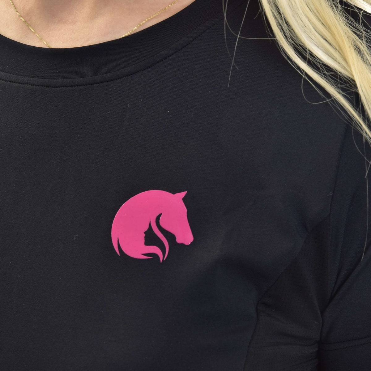 Close-up of the pink horse head logo on a black round-neck sports top, worn with a thin gold necklace