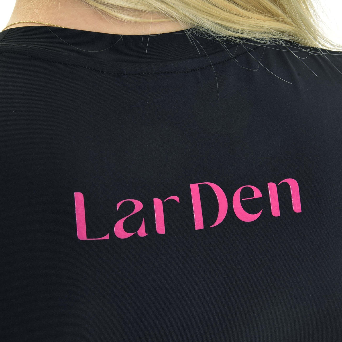 Close-up of the pink LarDen lettering on the back of a black round-neck sports top, blonde hair over the shoulder
