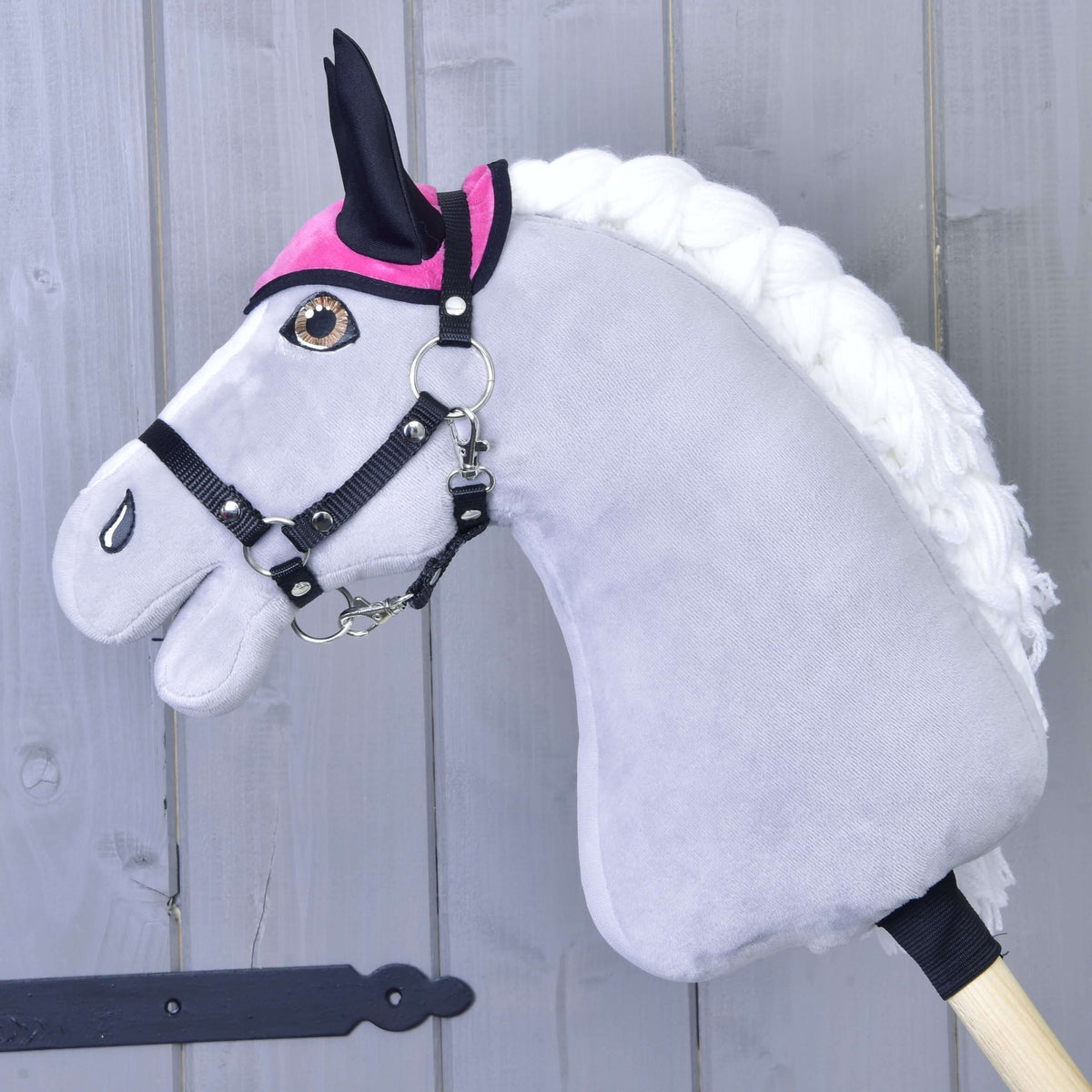 Szürke Hobby Horse ló fekete kötőfékben, rajta csak az élénk rózsaszín fülvédő fekete fülekkel