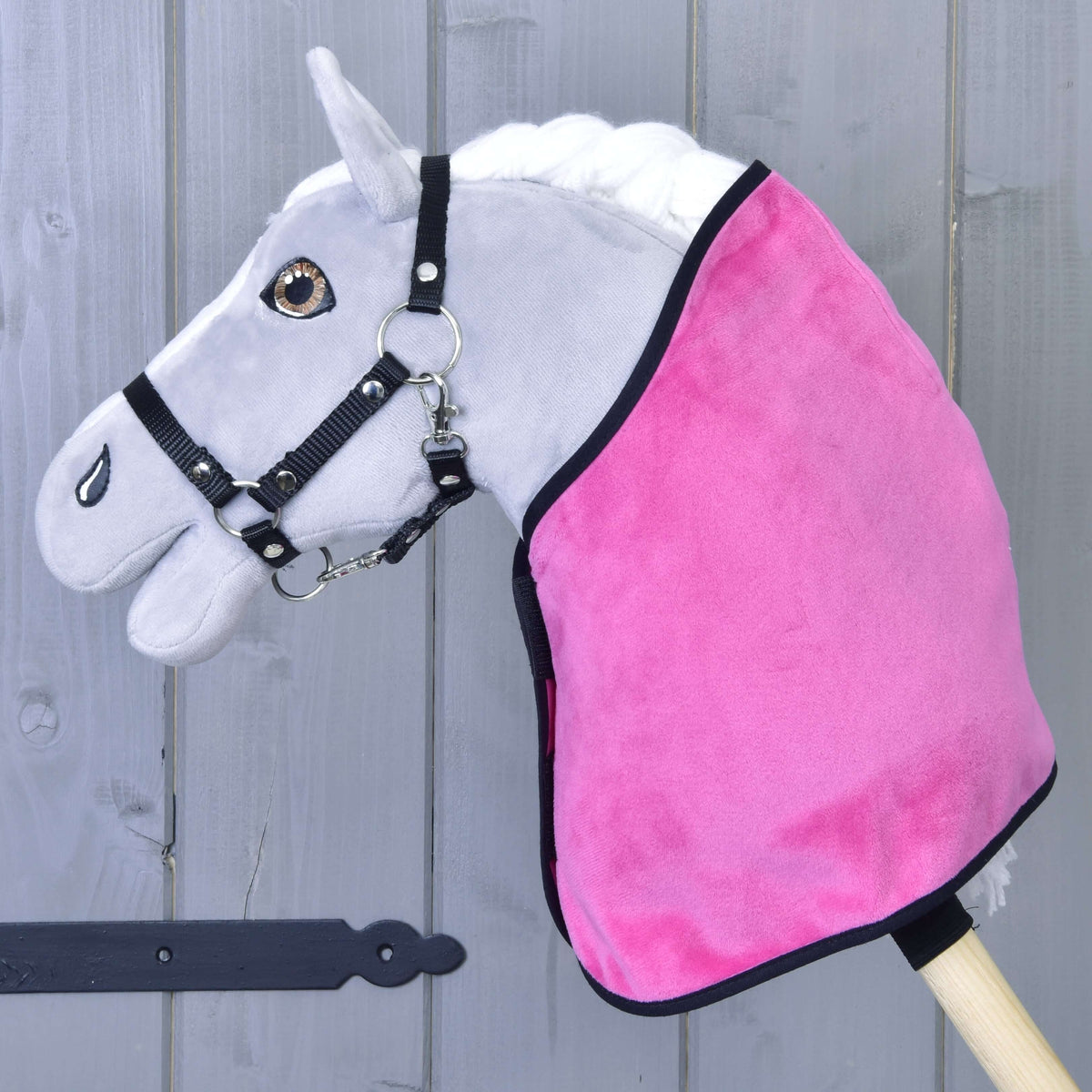 Szürke Hobby Horse ló fekete kötőfékben, rajta csak az élénk rózsaszín bársonyos takaró fekete szegéssel