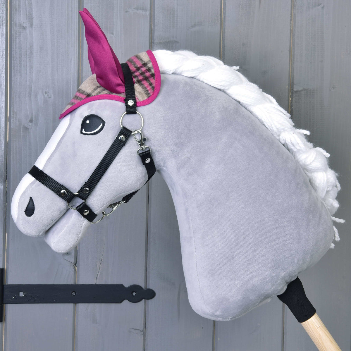 Szürke Hobby Horse ló fekete kötőfékben, rajta csak a kockás fülvédő rózsaszín fülekkel és rózsaszín szegéssel
