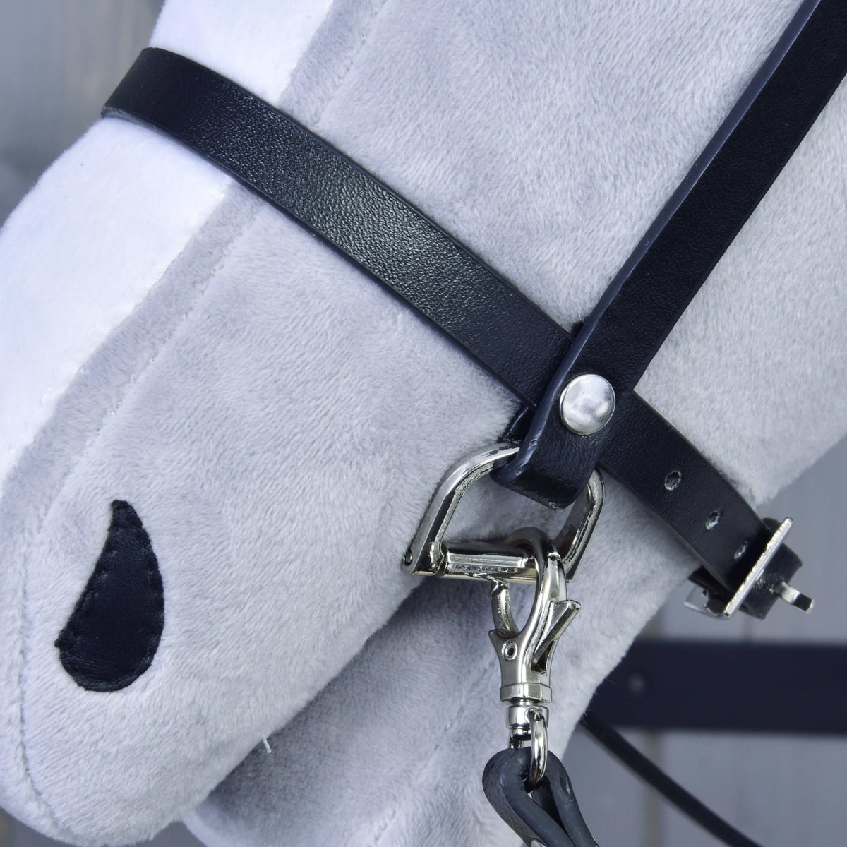 Részlet: fekete műbőr orrszíj ezüstszínű D-karikával és a kantárszár karabinere egy világosszürke Hobby Horse ló orrán