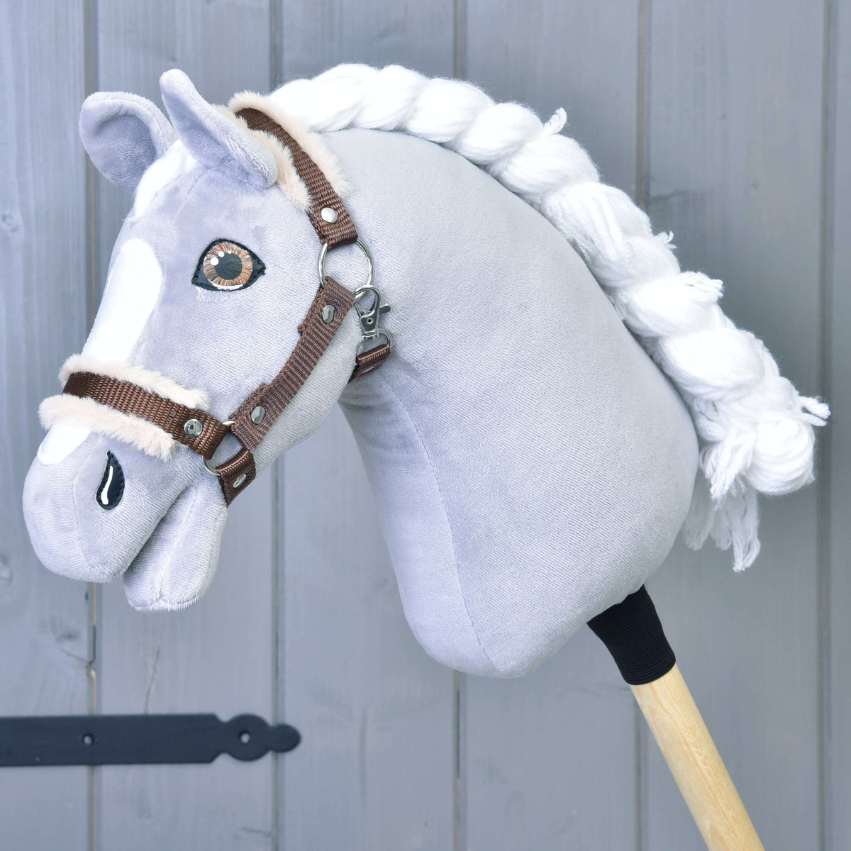 Szürke plüss Hobby Horse ló fonott fehér sörénnyel és barna szemekkel, rajta a barna kötőfék bézs szőrmével
