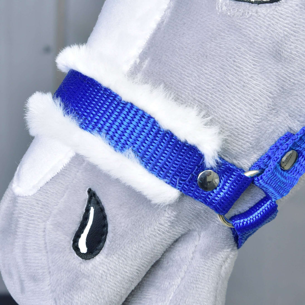Közeli kép: királykék orrszíj puha fehér szőrmebéléssel és ezüstszínű szegeccsel, szürke plüss Hobby Horse lovon