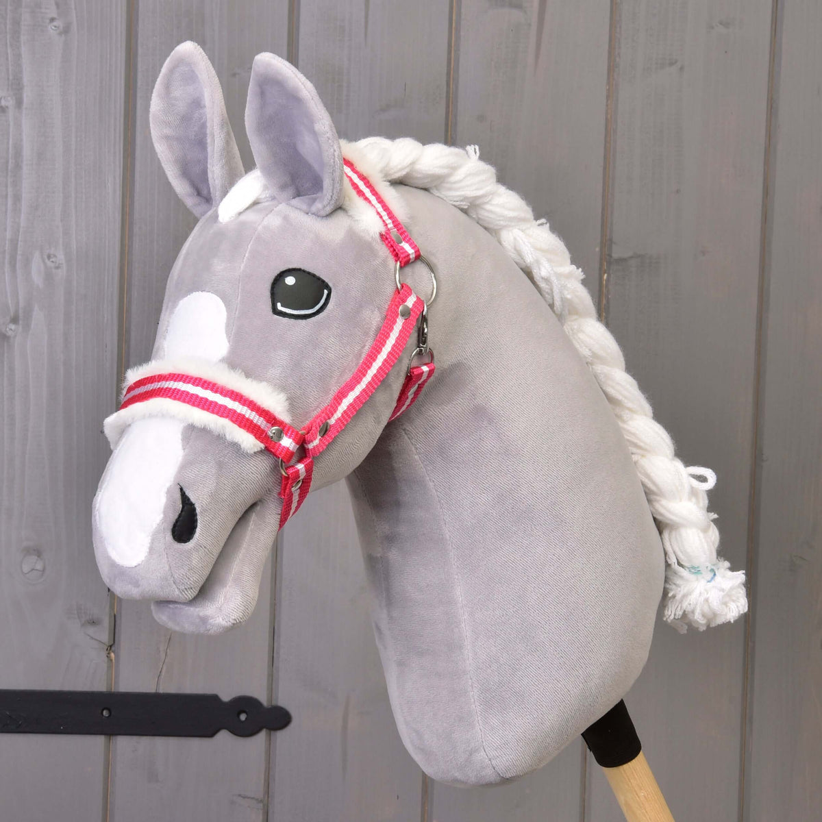 A grey plush Hobby Horse with a white blaze and braided mane wears the red striped halter with white fur