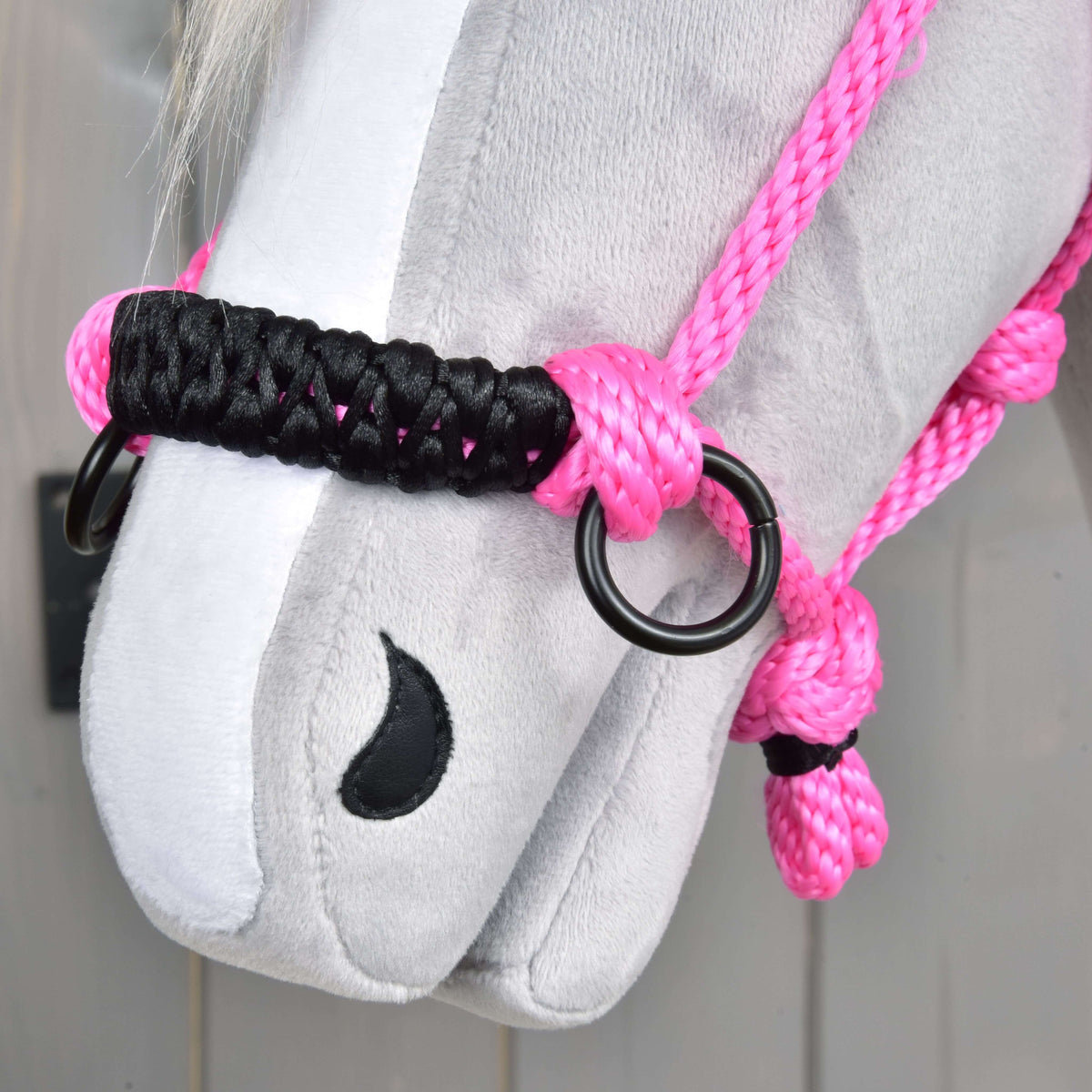 Close-up of the black braided noseband with black rings on the pink rope halter, resting on a grey plush muzzle