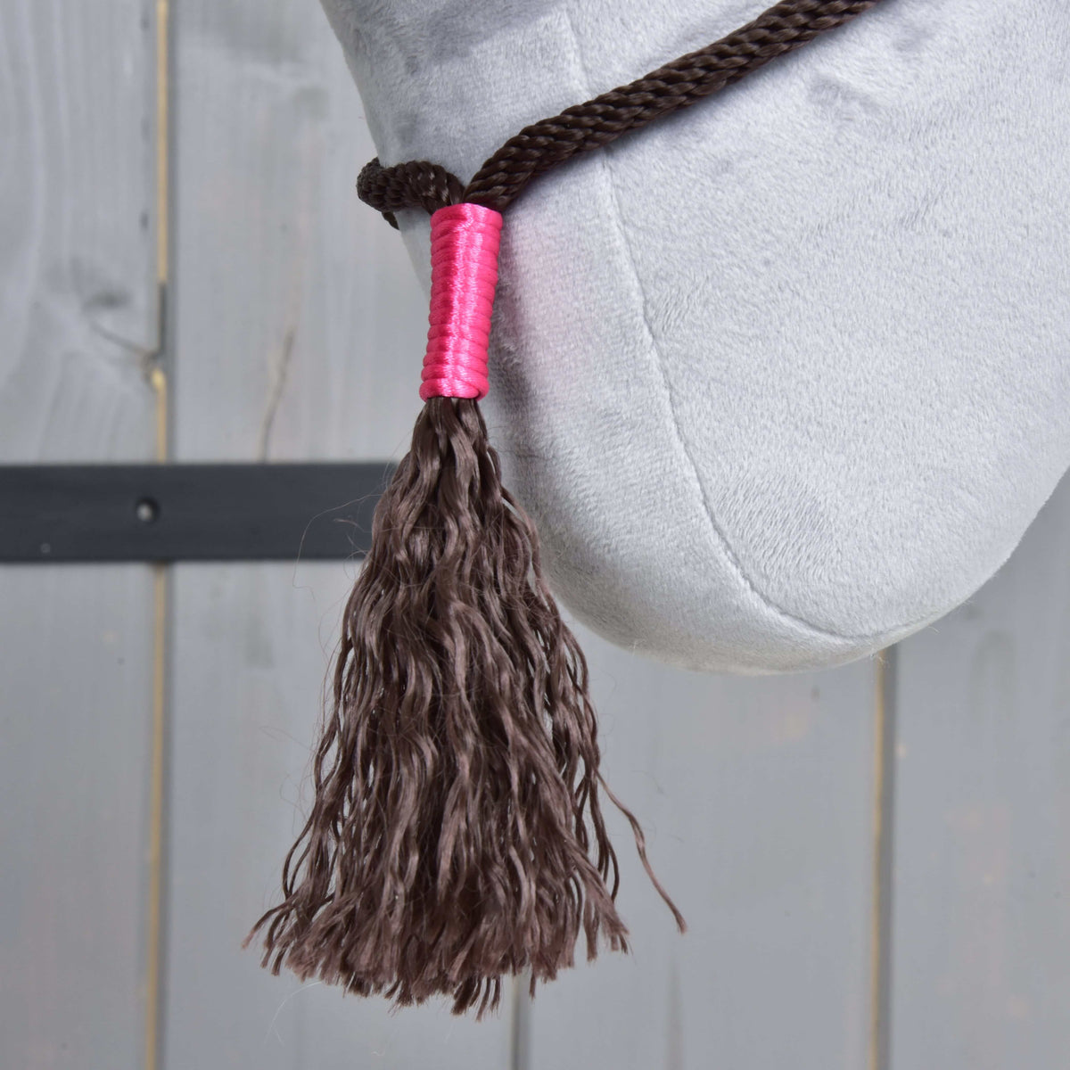Close-up of the wavy brown tassel with a bright pink wrap from Rope set Noir Cocoa, hanging below a grey plush jaw