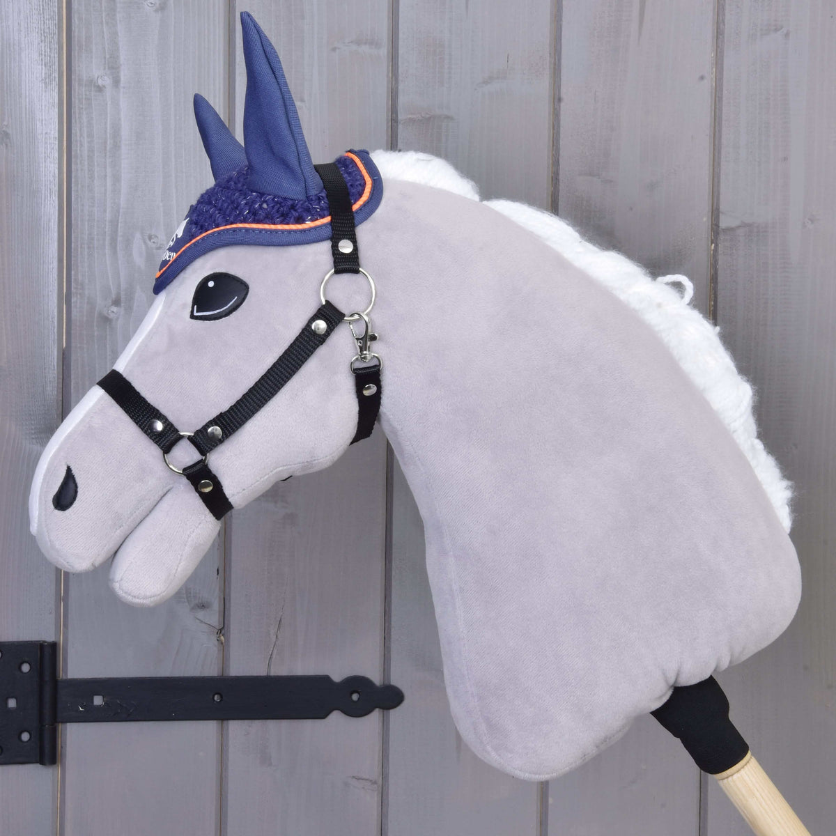 Fehér sörényű szürke Hobby Horse ló oldalnézetből, fekete kötőfékkel és a horgolt Blue Sport fülvédővel