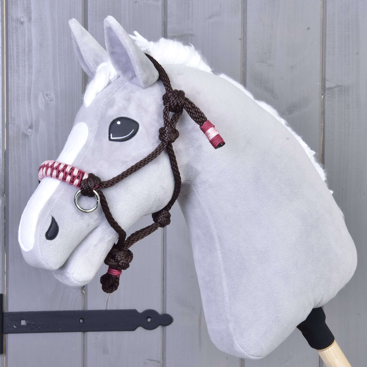 Szürke plüss Hobby Horse ló a sötétbarna York csomózott kötőfékben, rózsaszín-bordó fonott orrszíjjal