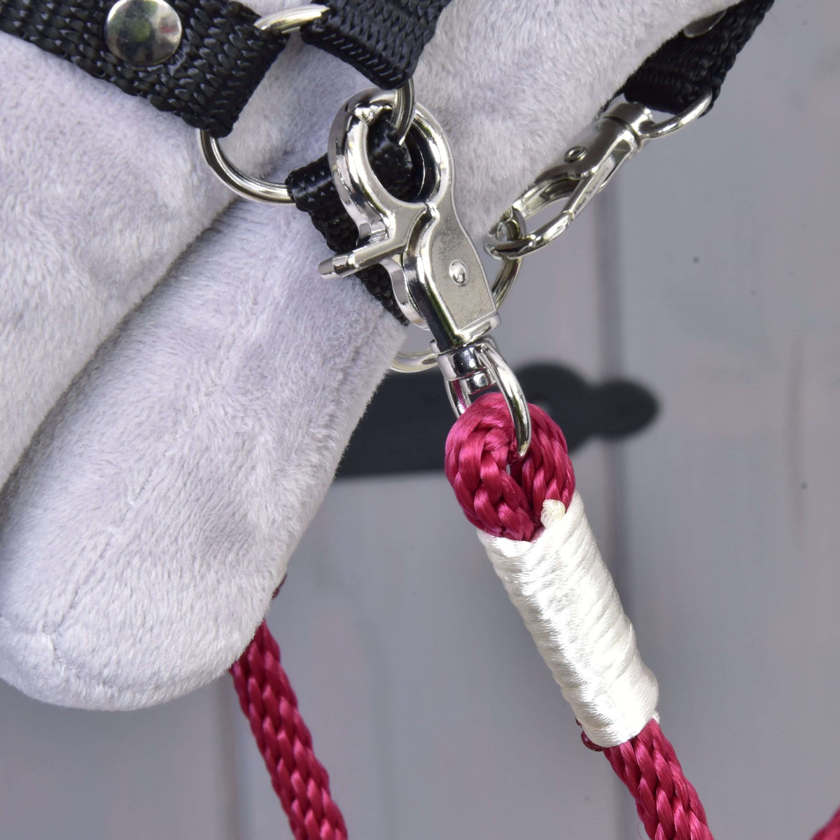 Close-up of the silver snap hook and glossy white wrap on the burgundy Czi-czi rope reins at the halter of a Hobby Horse