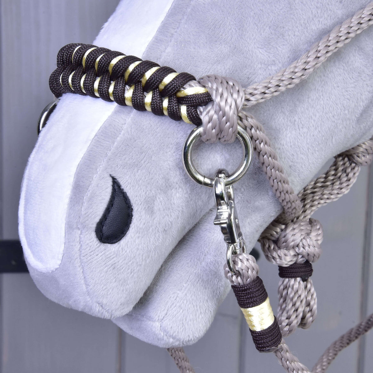 Close-up of the dark brown and gold braided noseband, snap hook and wrapped rein end of Rope set Splendid on a Hobby Horse