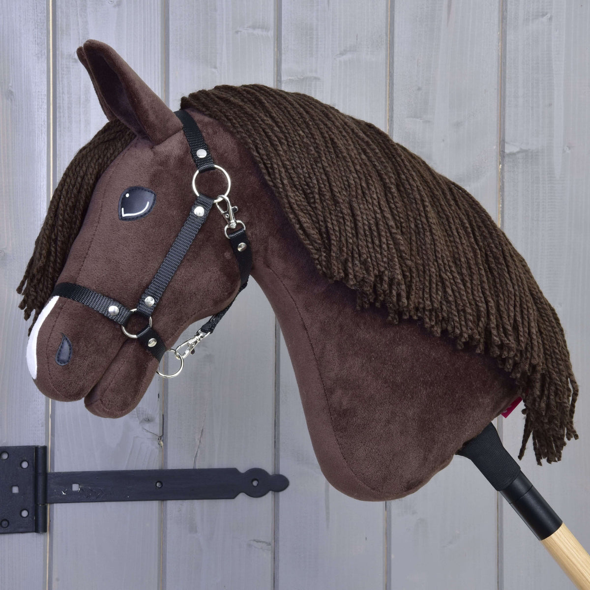 A sötétbarna Hobby Horse ló oldalnézetből, hosszú barna fonalsörénnyel és fekete nejlon kötőfékkel, karabinerrel