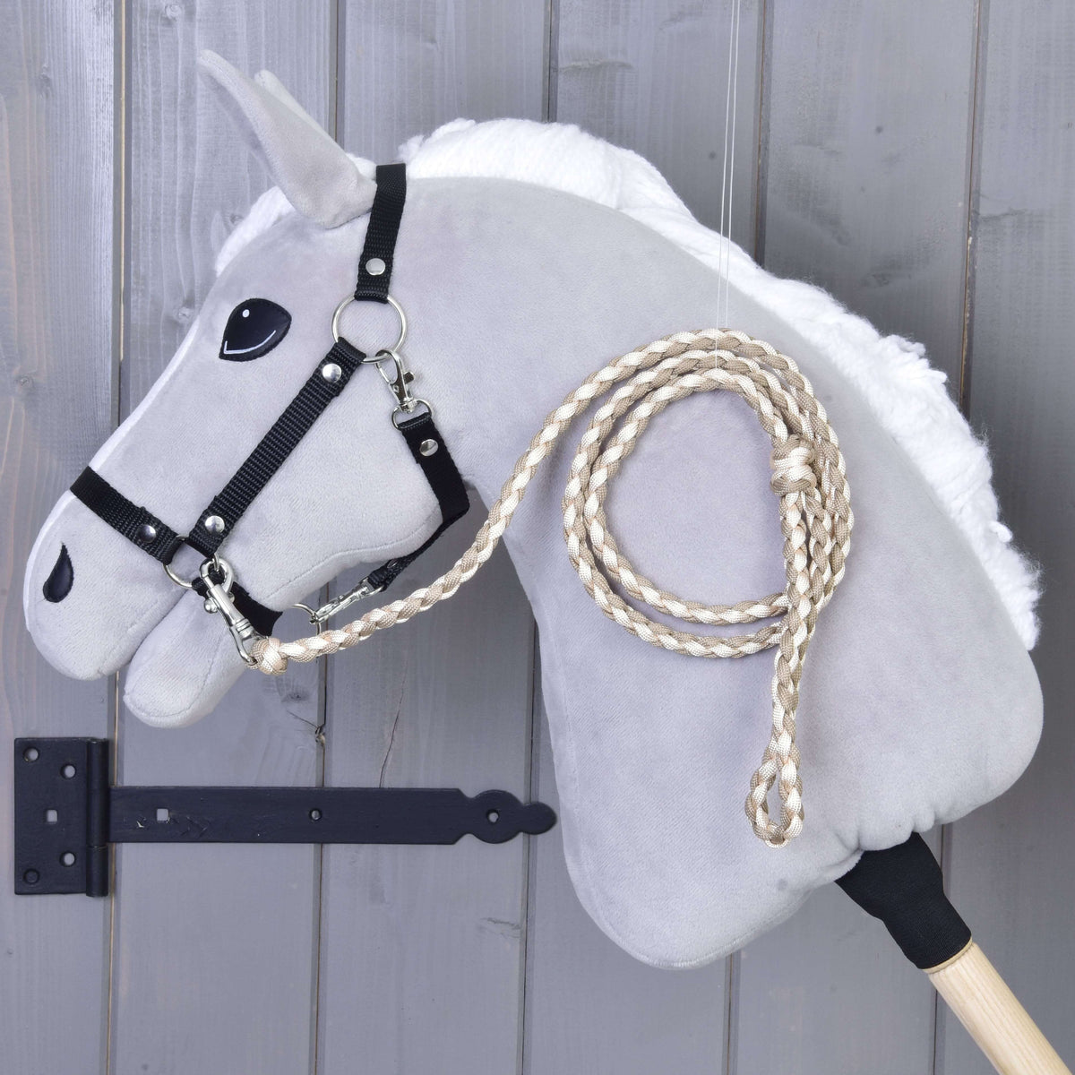 Krémszínű-bézs fonott vezetőszár egy szürke Hobby Horse ló fekete kötőfékére csatolva, szürke fafal mellett