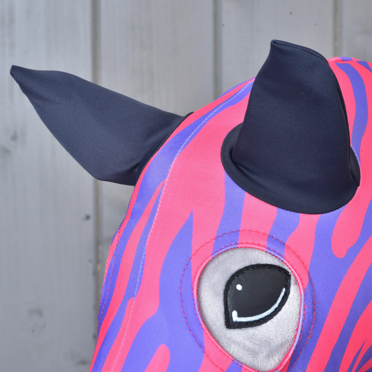 Close-up of the Hobby Horse protective suit Fancy on a plush head: navy fabric ears and an eye opening framed by zebra stripes