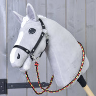 Világosszürke Hobby Horse ló fekete kötőfékben, a nyaka körül a fekete-piros-sárga fonott Flag kantárszár
