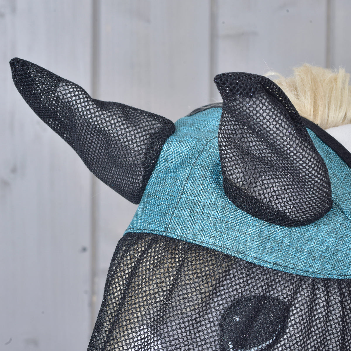 Közeli kép a légymaszk fekete hálós fülrészeiről és texturált türkiz fejtetőbetétjéről egy szürke Hobby Horse lovon
